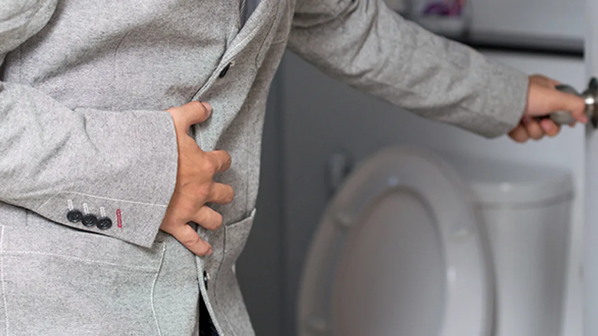 A man standing at a toilet with one hand pressed to his lower back